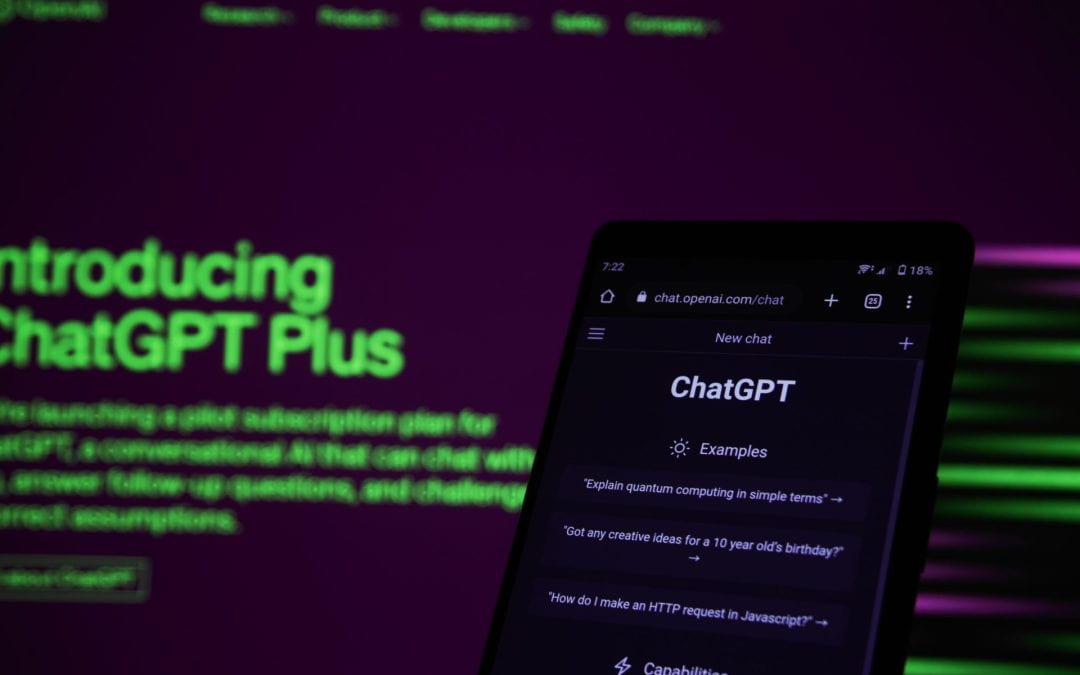 A smartphone displaying ChatGPT positioned in front of an illuminated computer screen introducing ChatGPT plus.
