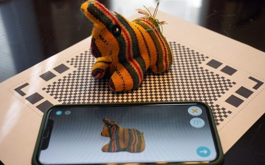 A toy sits on a scanning mat, with a phone in the foreground with the captured image.