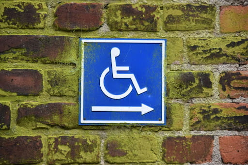 A brick wall with a small square wheelchair accessible sign and arrow pointing right.